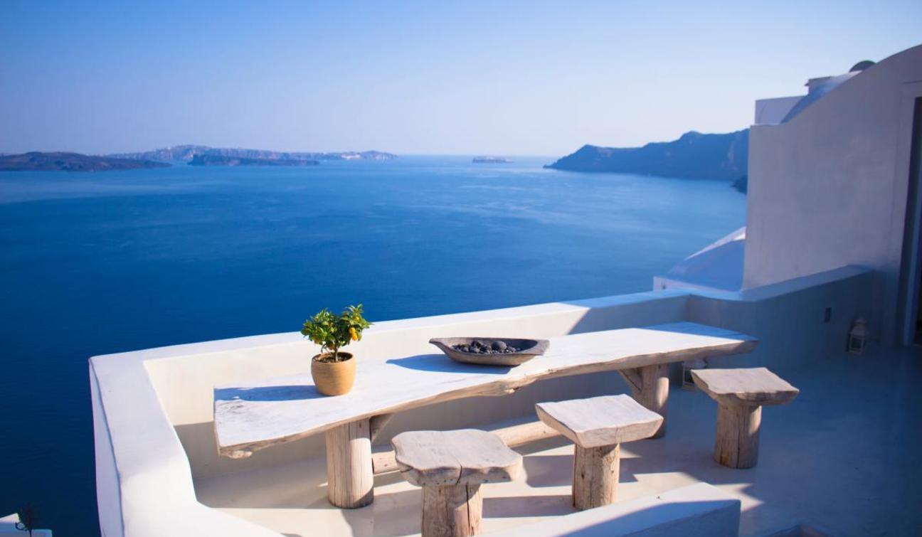 Exclusive dining setup with modern design on a white patio that overlooks the Mediterranean Sea's blue water in Oia, Greece.