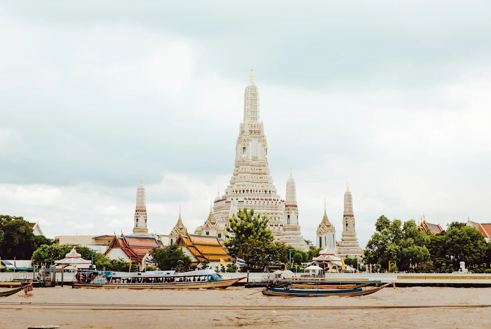 A view of temples with red and yellow roofing and intricate stonework in Bangkok surrounded by green trees.