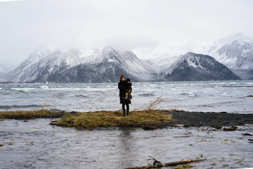 a woman and her child on a small patch of grass in a lake on a cold foggy day