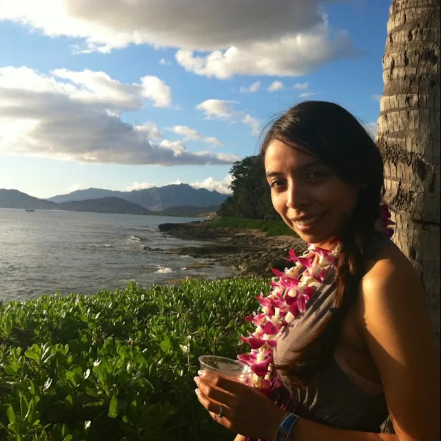 Travel Advisor Alicia Zepeda with a lei standing in front of a green mountain scape with water.