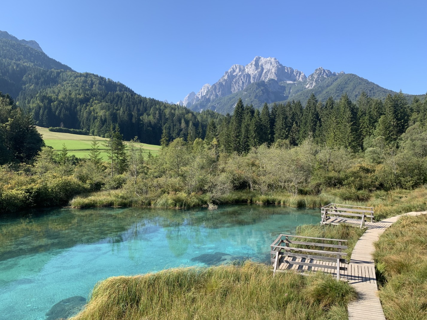 Blue body of water next to wooden path with mountains in the background during daytime