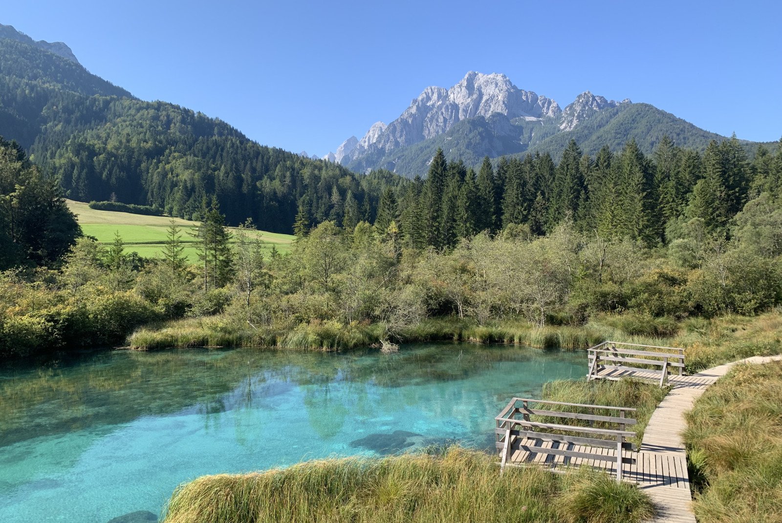 Blue body of water next to wooden path with mountains in the background during daytime