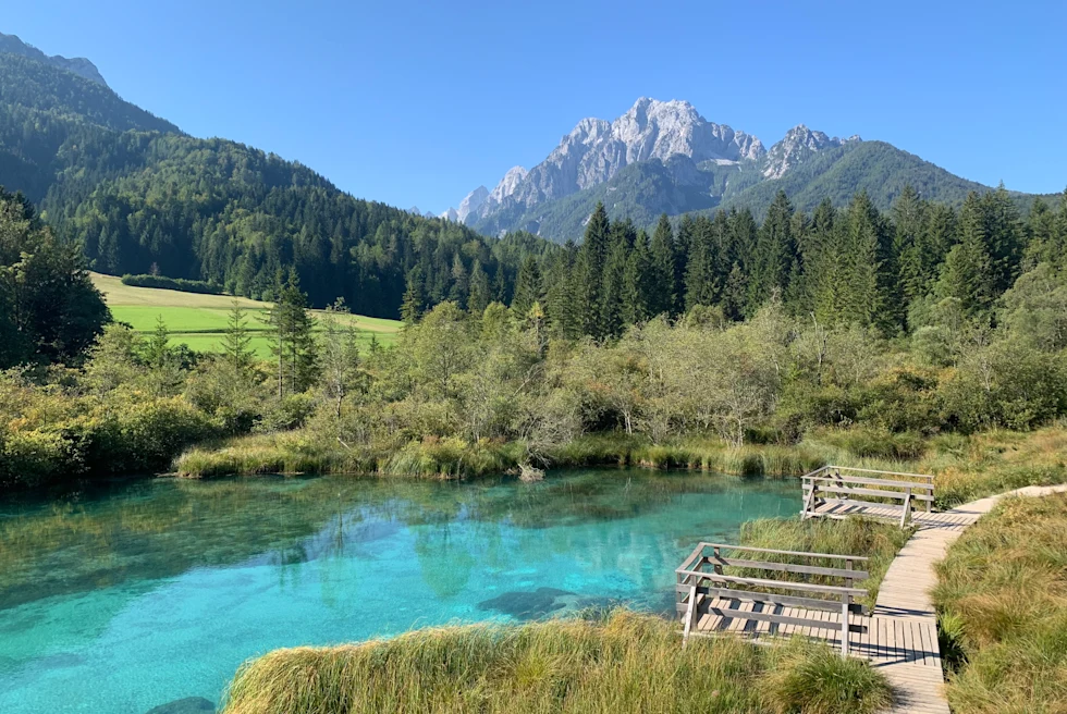 Blue body of water next to wooden path with mountains in the background during daytime