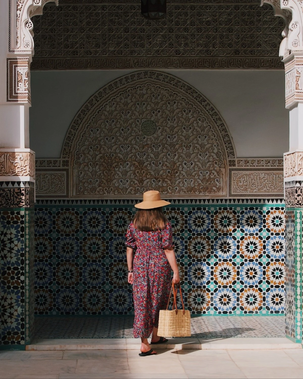 woman in a hat walks beneath a colorful archway