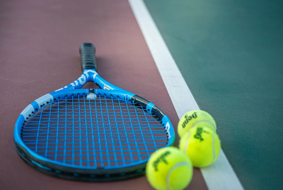 blue tennis racket on a court with two tennis balls