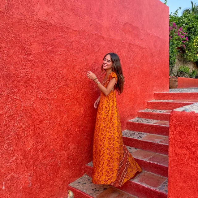 woman wearing orange dress standing next to red wall