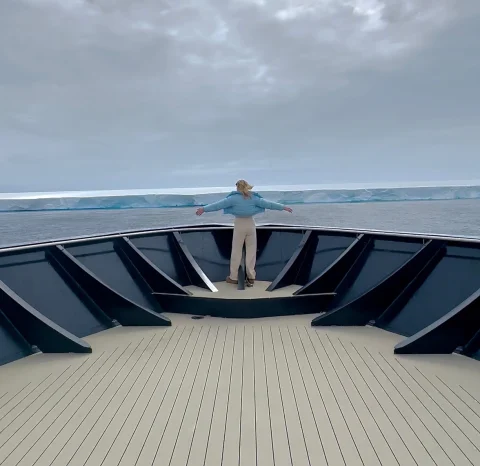 A person standing at the end of a boat looking out to sea