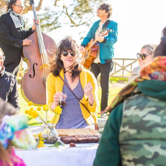 Travel Advisor Karen Cook in a purple dress and yellow sweater with musicians playing in the background.