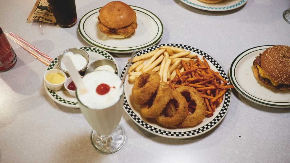 Burgers with a milkshake and onion rings on a white-cloth table. 