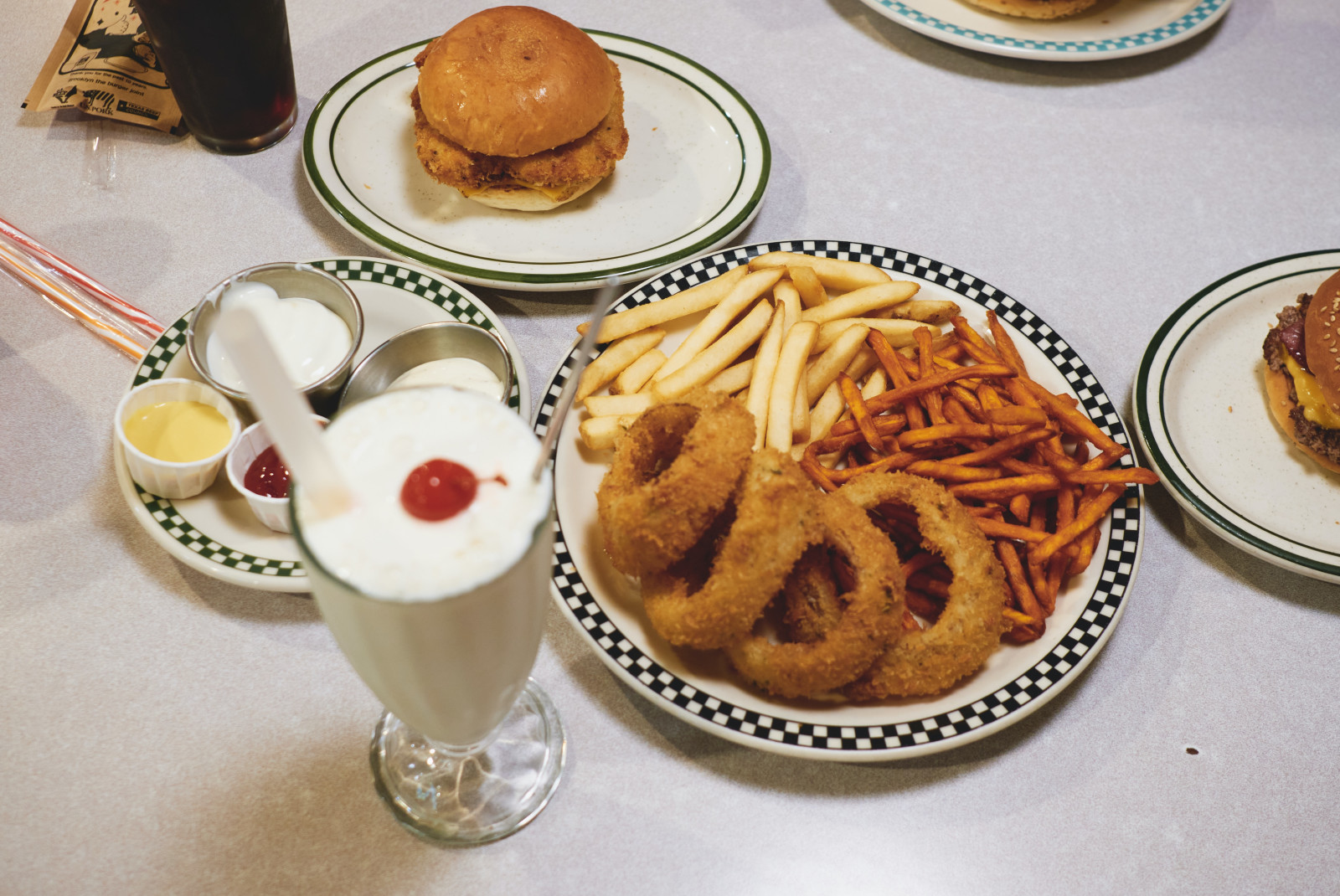 Burgers with a milkshake and onion rings on a white-cloth table. 