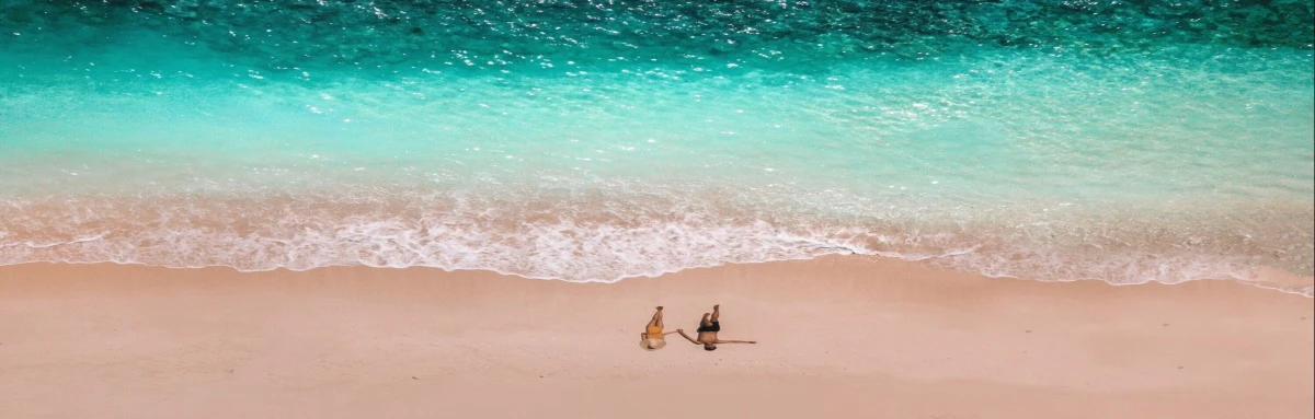 Couple holding hands and walking on a romantic private shore with turquoise ocean waters and white sands in the Bahamas.