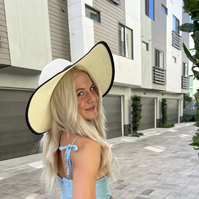 Travel advisor Maddy Mazzeo wears a blue dress and large brim sun hat on a quiet city street