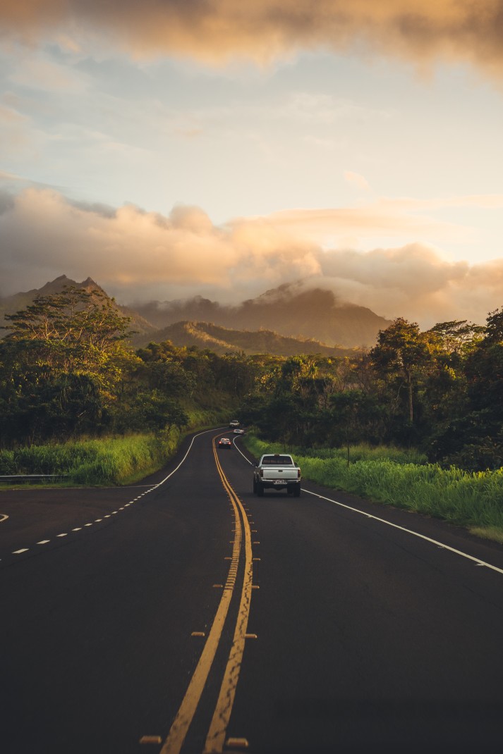 A paved road with a white truck driving into green mountains into the distance in Maui, Hawaii.