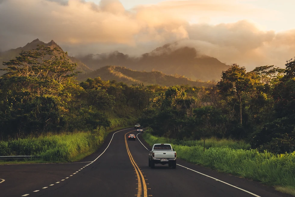 A paved road with a white truck driving into green mountains into the distance in Maui, Hawaii.