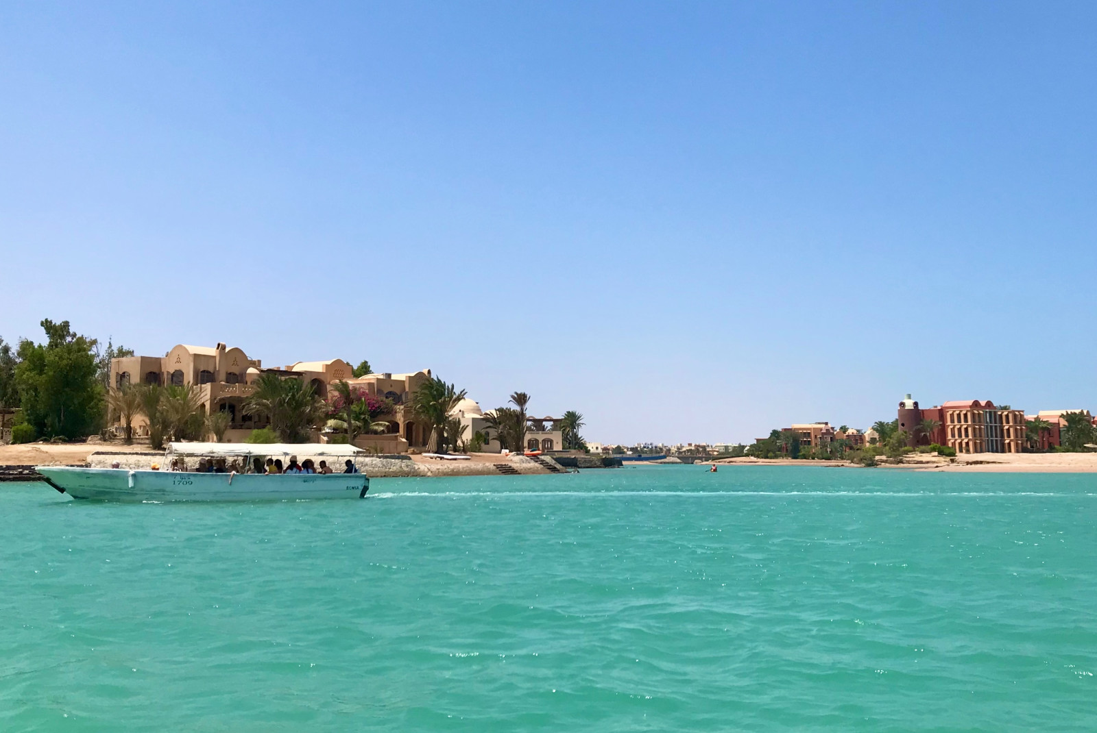 Blue water with boat and buildings and trees with a blue sky