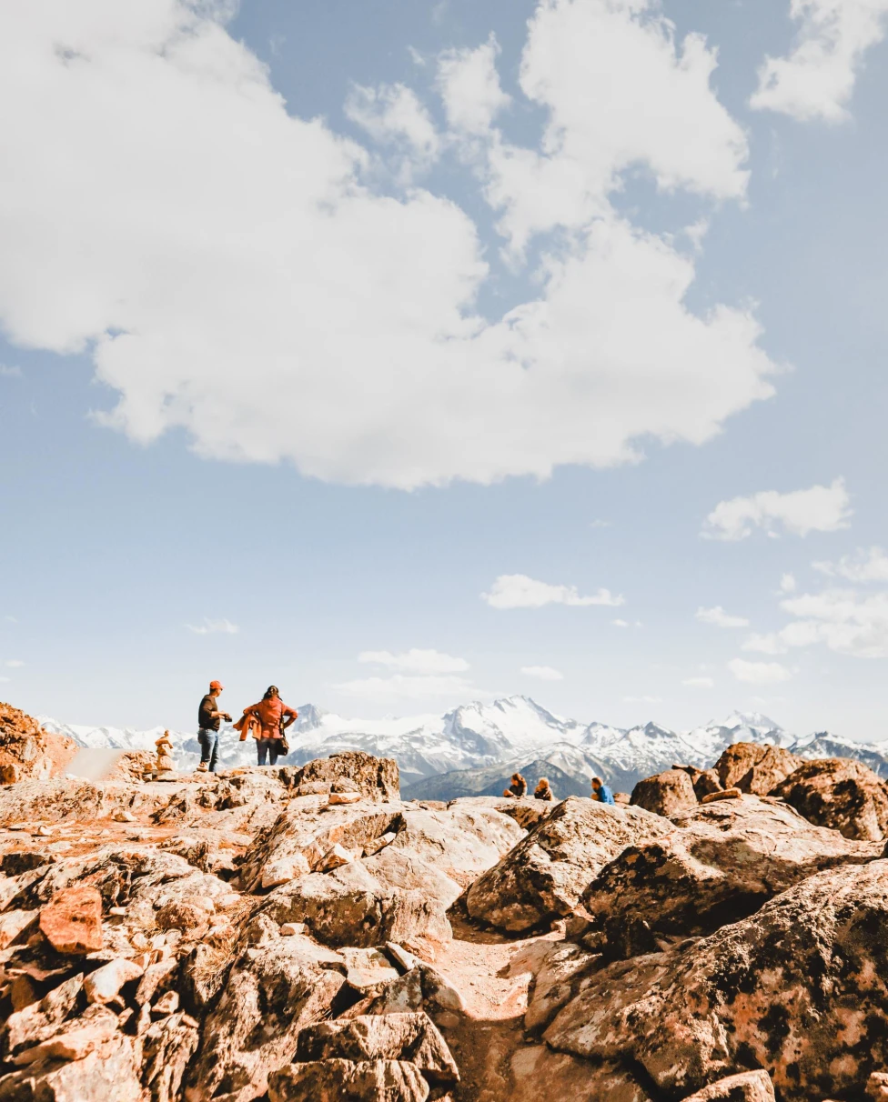 people stand on rock cliff at the peak of a mountain on a clear sunny day 