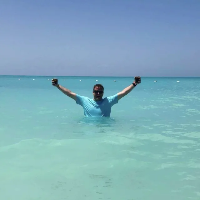Travel advisor Michael in a blue shirt standing in water with his arms outstretched above him. 