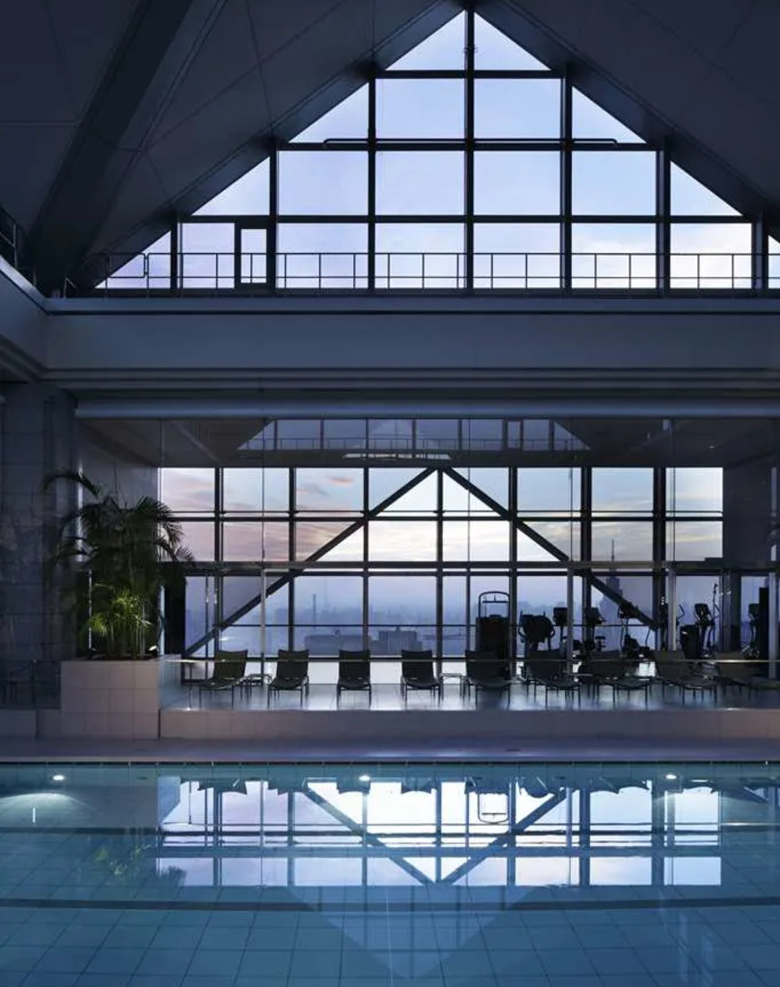 a pool in an atrium with glass ceilings and a large window overlooking a city