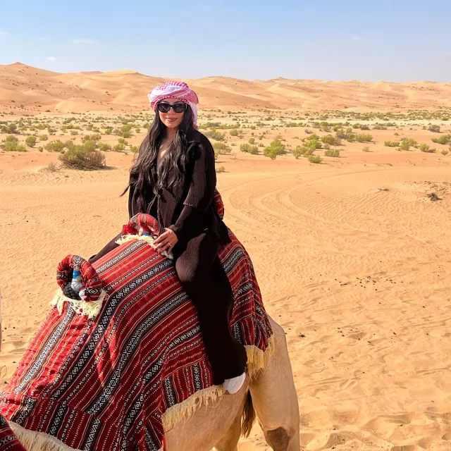 Picture of Alma riding a camel in the desert.