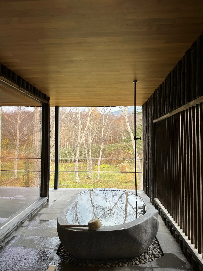 The Zaborin onsen, with a tub in the center of a stone and wood room overlooking a field with trees