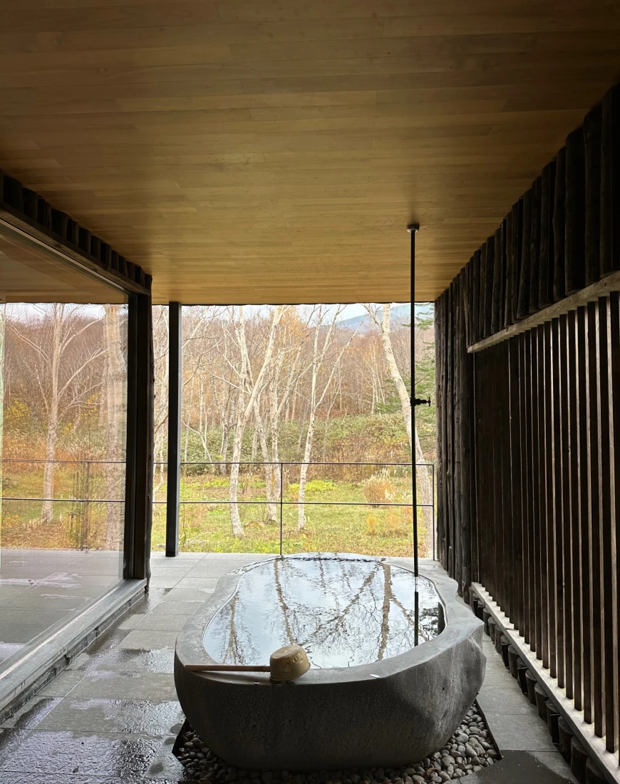 The Zaborin onsen, with a tub in the center of a stone and wood room overlooking a field with trees