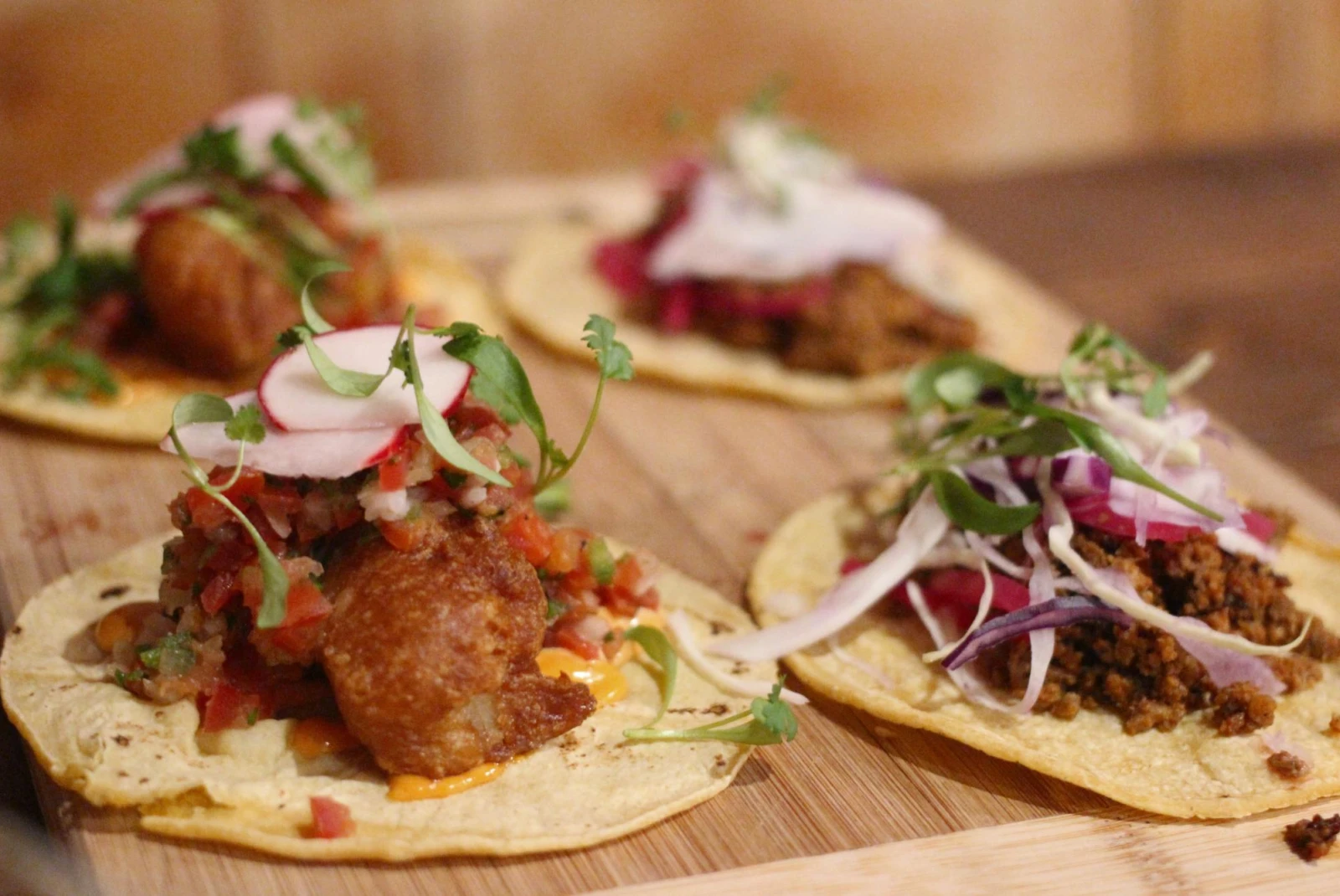 Fancy tacos laid flat on wooden board on table in stylish restaurant.