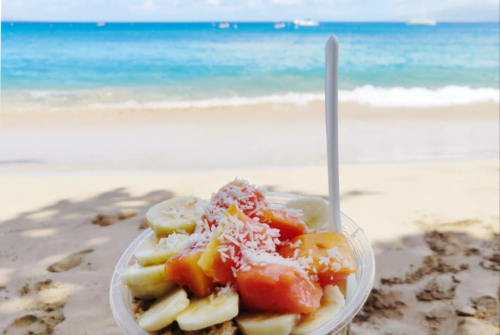 plastic bowl filled with fruits with the ocean in the background