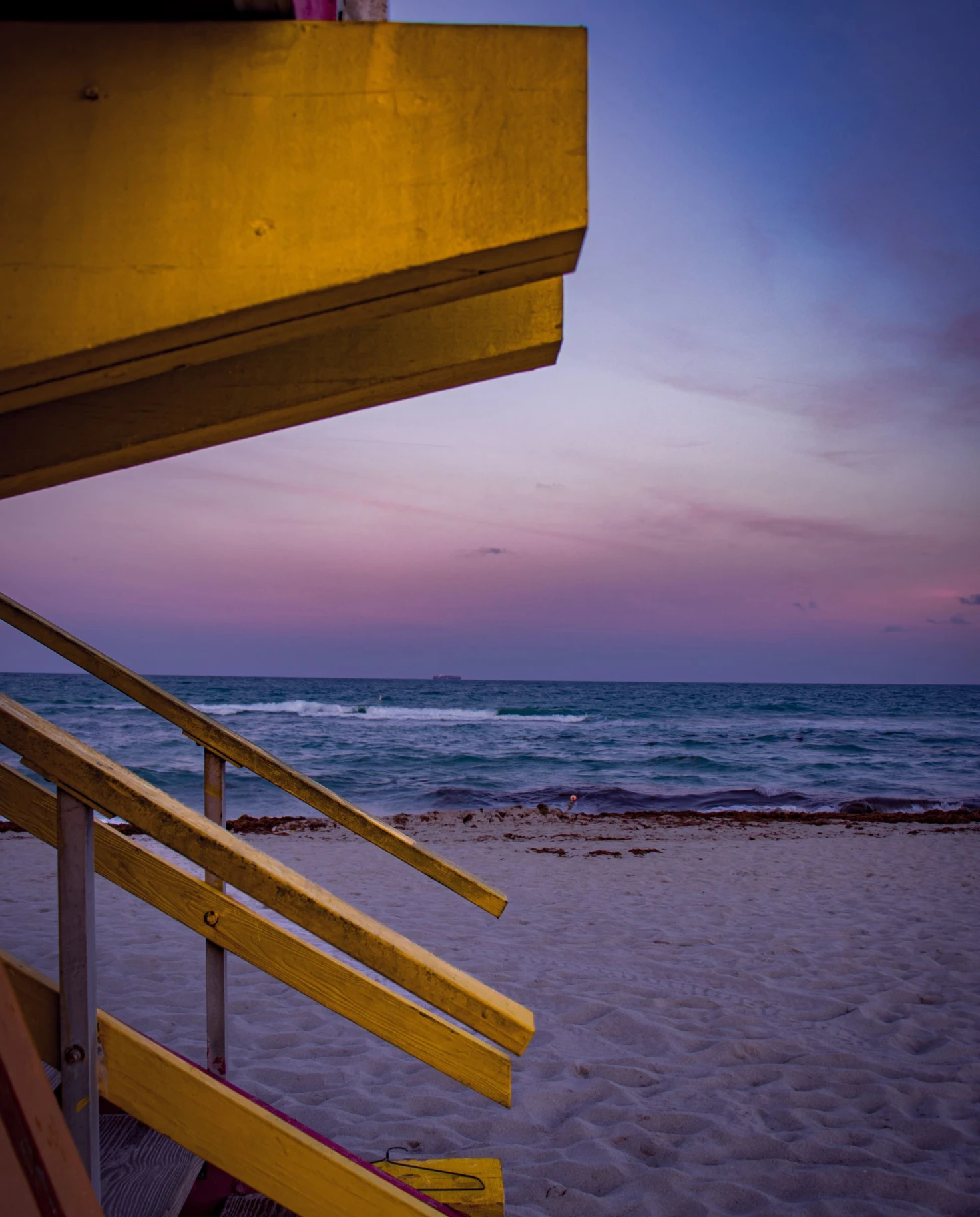 purple sunset on the beach next to yellow lifeguard stand