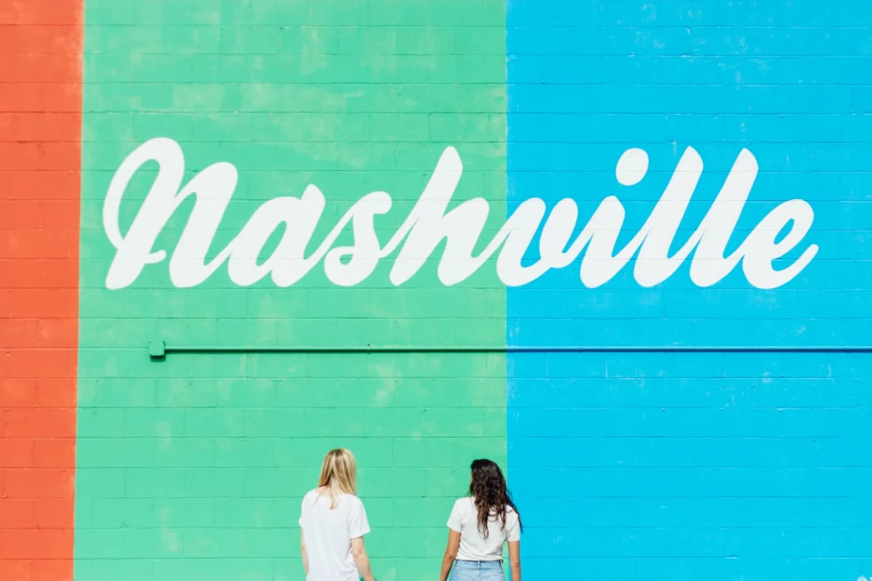 Two women facing wall with nashville written on it. 