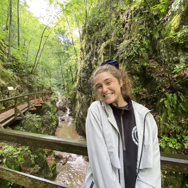 Anna Marie DuHamell posing for a photo outside in front of green trees on a wooden bridge