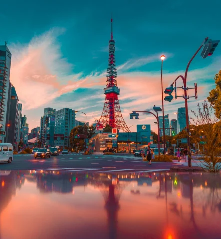 A view of a red tower and city skyline in Tokyo with pink clouds and a blue sky in the background. 