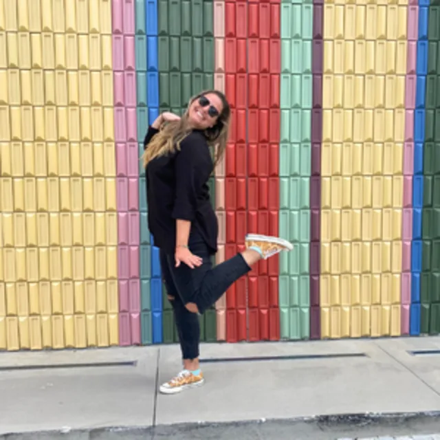 Travel Advisor Andrea Mujica in jeans and a black shirt in front of a colorful wall.