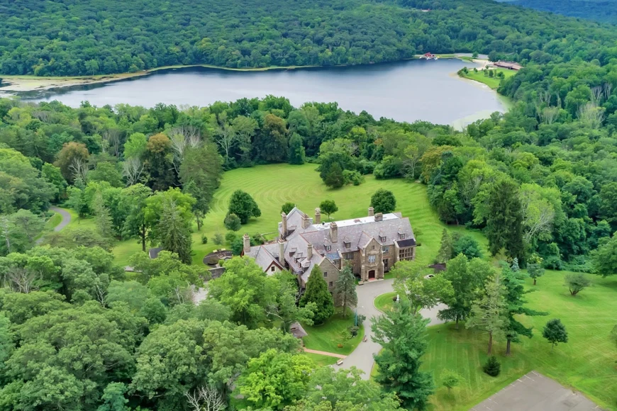 aerial view of a stone mansion in a lush forest near a lake