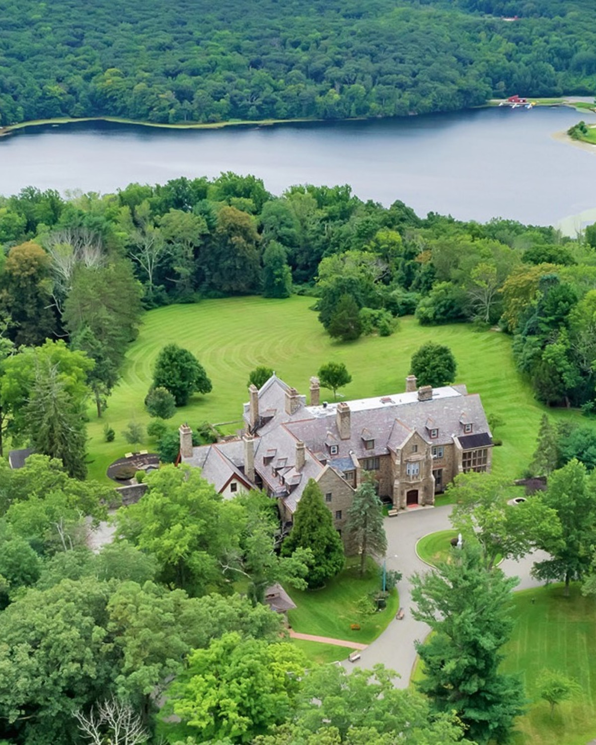 aerial view of a stone mansion in a lush forest near a lake