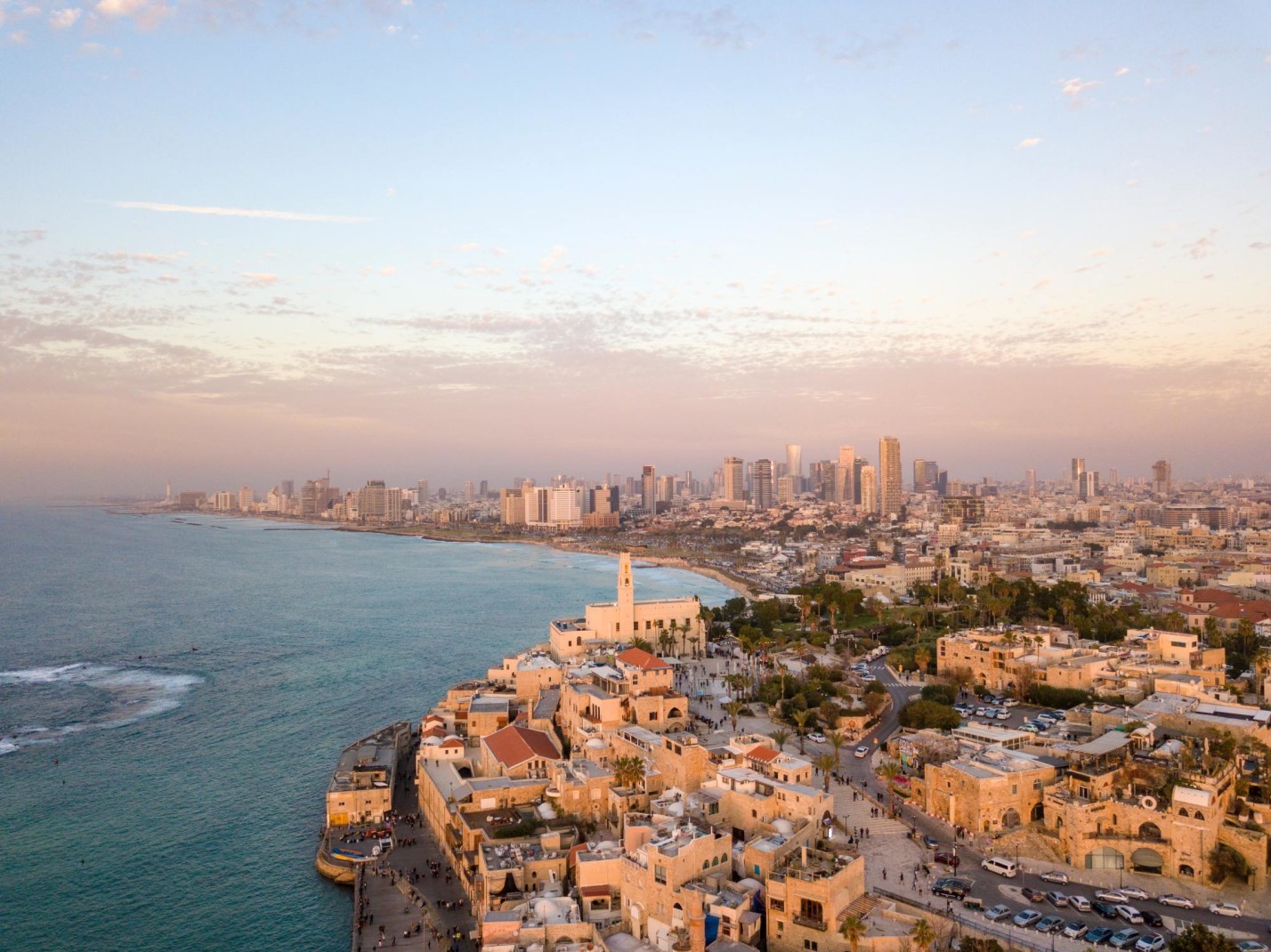 City with modern and historic buildings, Tel Aviv, next to ocean as the sun sets.