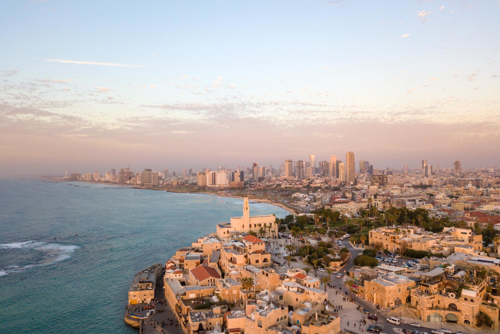 City with modern and historic buildings, Tel Aviv, next to ocean as the sun sets.