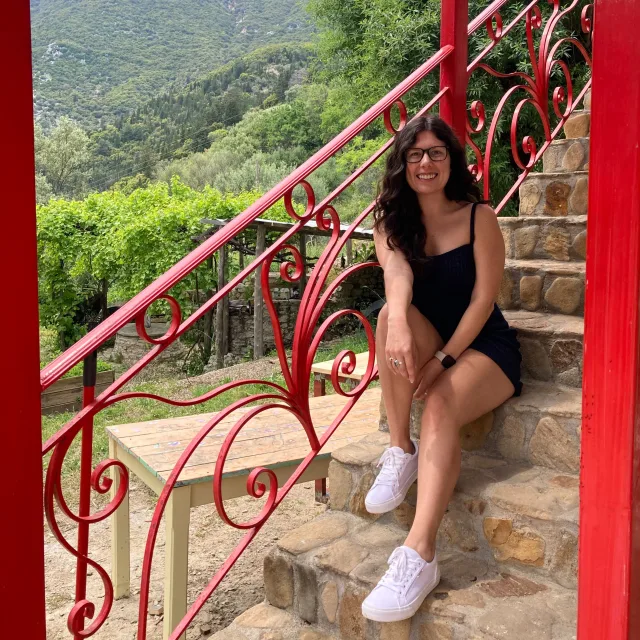 Travel advisor sitting on a staircase wearing black top and white sneakers.