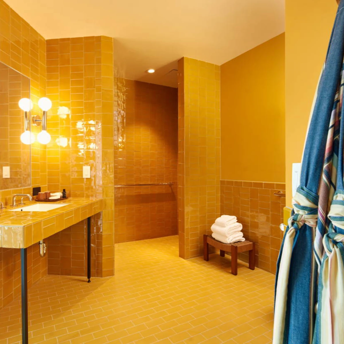 colorful robes hanging in a yellow tiled bathroom