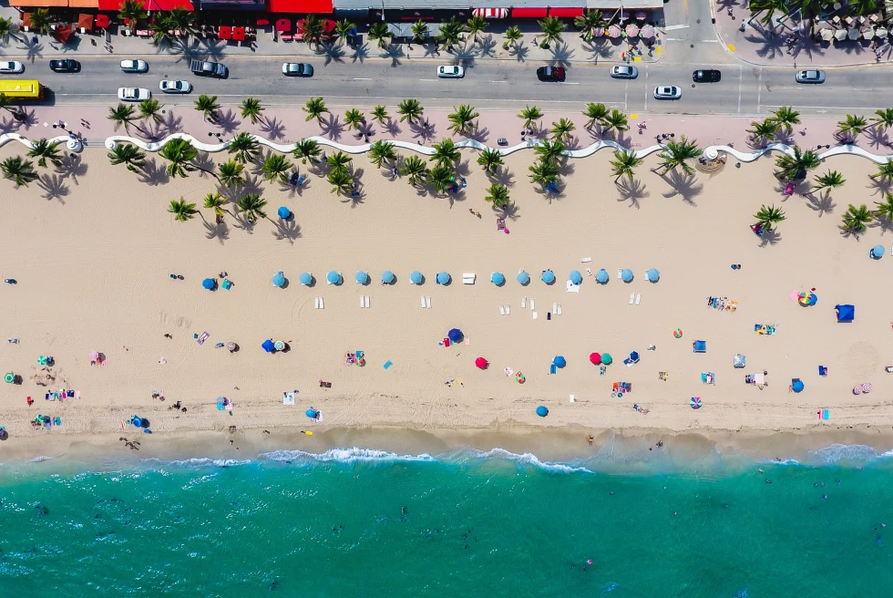 A beach view at Fort Lauderdale showing traffic on the roadside and people relaxing on the beach.