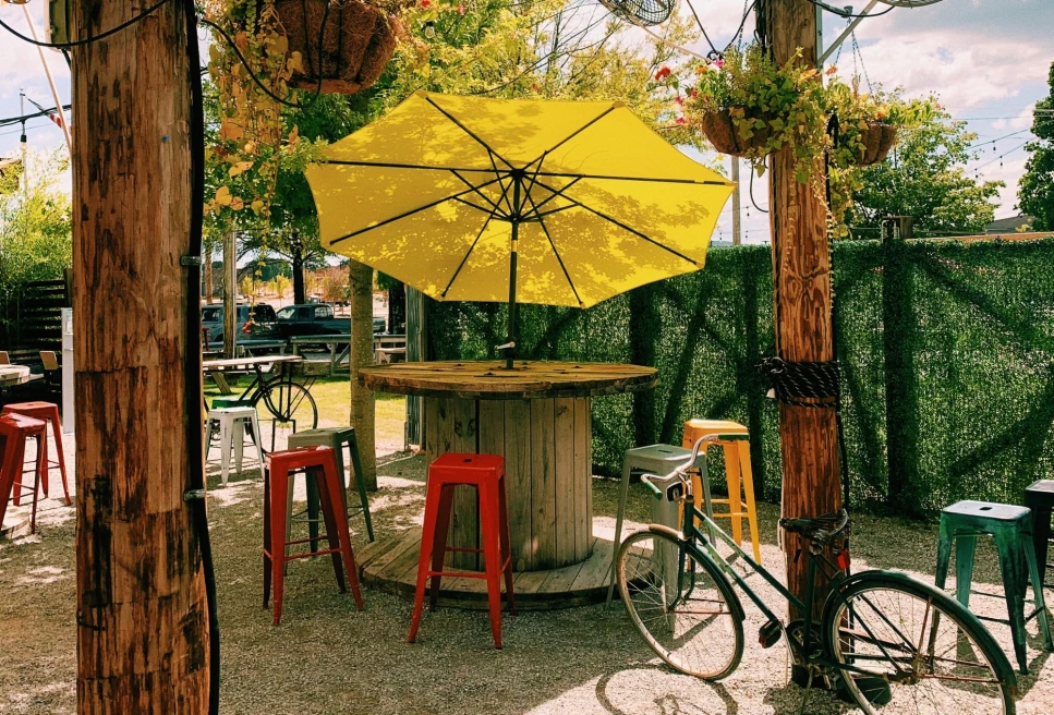 yellow umbrella and red stools at round tables on a bar patio