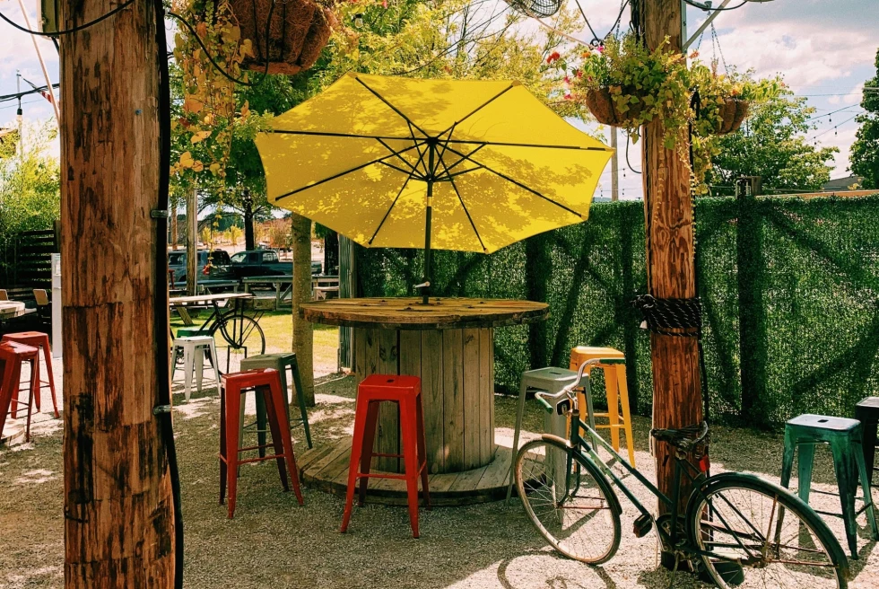 yellow umbrella and red stools at round tables on a bar patio
