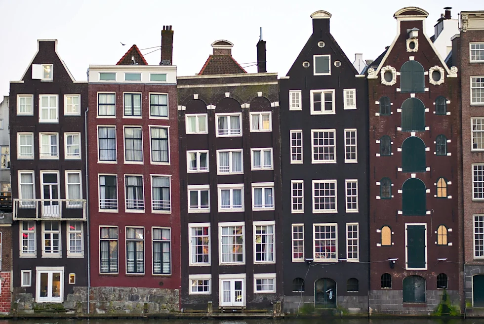 a row of old brown and red houses with six stories of big windows