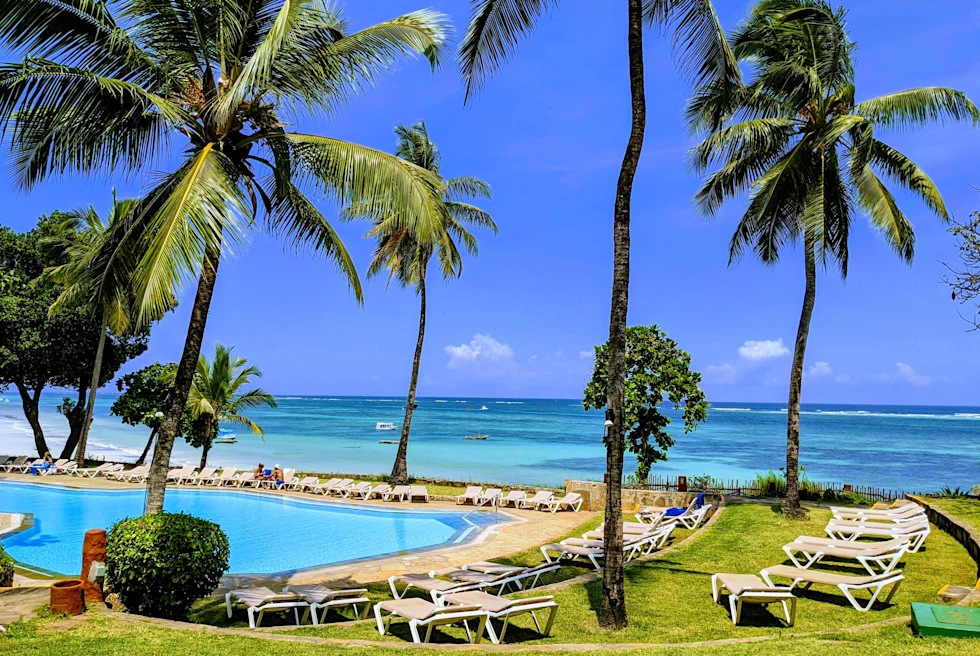 Lounge chairs and palm trees surrounding a pool next to the ocean on a sunny day in Kenya