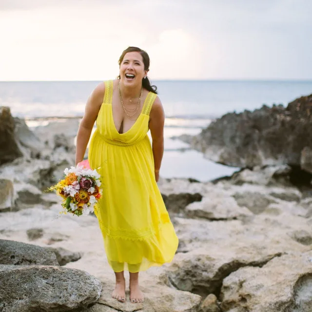 Travel advisor posing in a yellow dress holding flowers on a beach