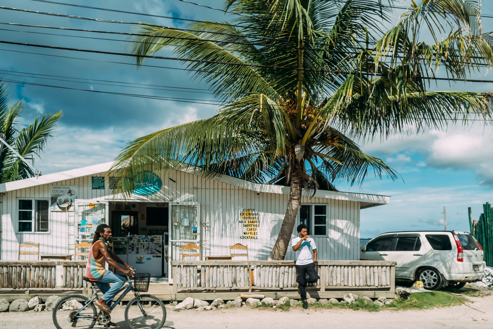 Man riding bike in front of white building next to palm tree during daytime