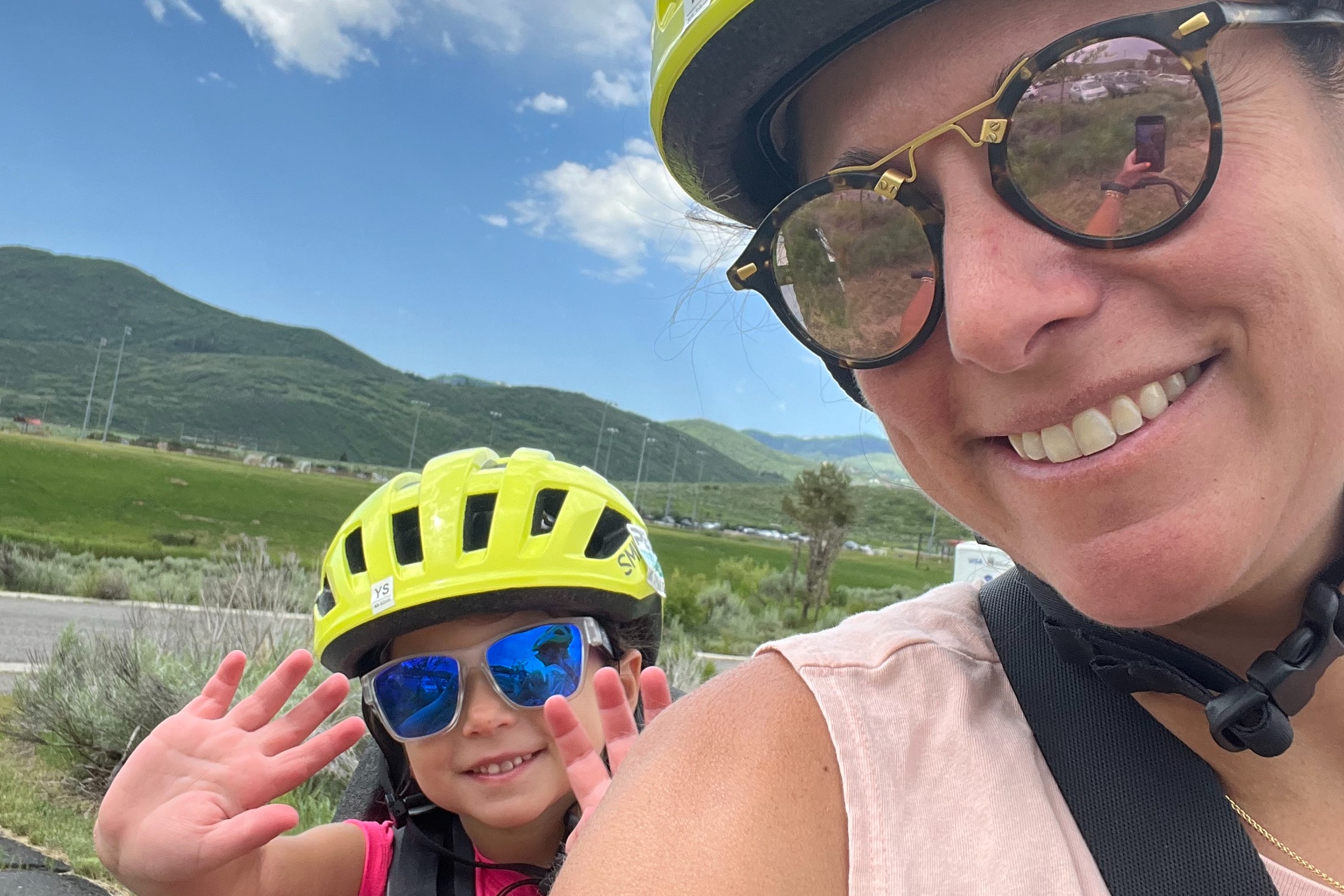 A woman and a kid wearing helmets and nd posing outdoors.