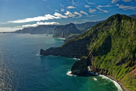 Overlooking green steep cliffs and blue waters crashing on the shores in Madeira, Portugal.