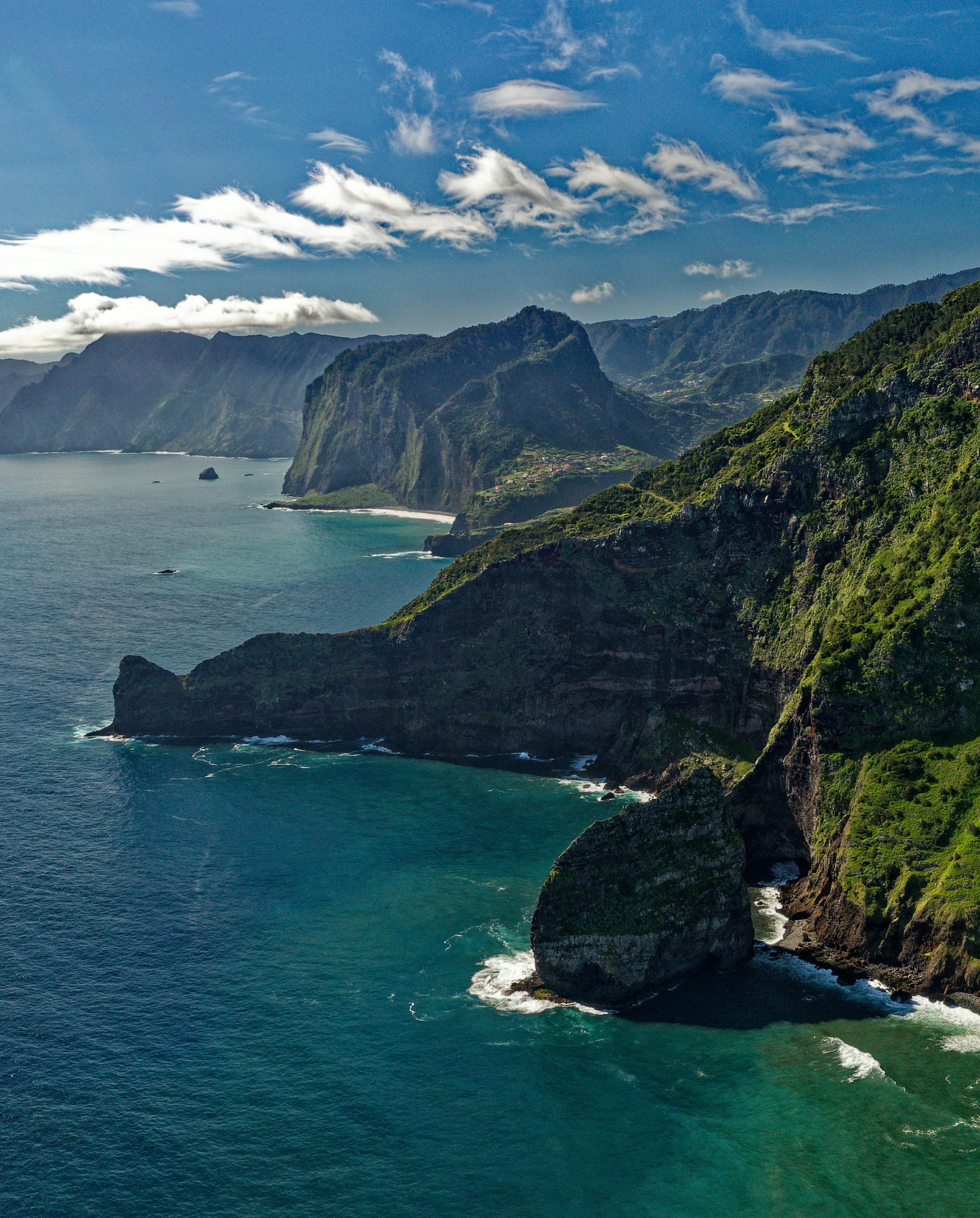 Overlooking green steep cliffs and blue waters crashing on the shores in Madeira, Portugal.