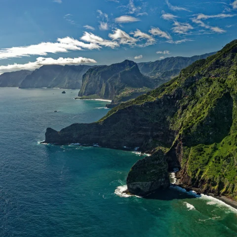 Overlooking green steep cliffs and blue waters crashing on the shores in Madeira, Portugal.