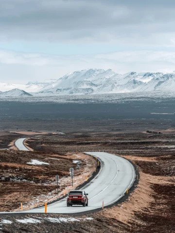 Car driving on winding road with mountains in the background and clouds in the sky